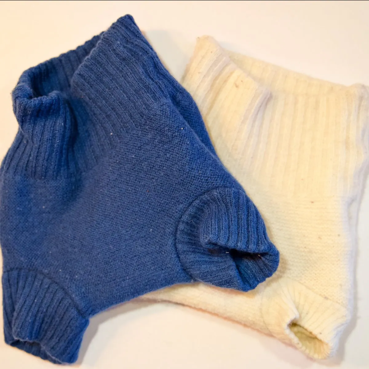 Zwei gestrickte Wollüberhosen in Blau und Naturweiss